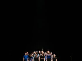 A group of children and teens stand together. Their heads are turned in various directions