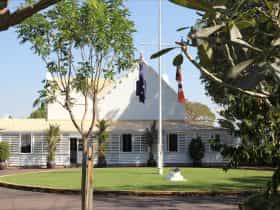 Front view of Government House with flag pole and frangipani tree in the foreground