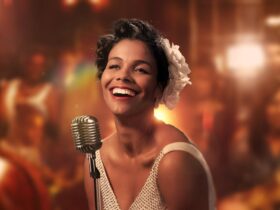 Zahra Newman wears a gardenia in her hair and smiled at the camera, stands in front of a vintage mic