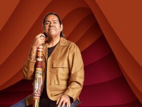 William Barton is smiling at the camera with his chin up, holding his didgeridoo against his chest