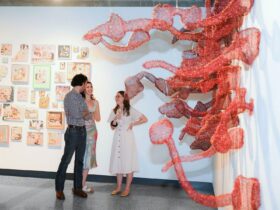 3 people standing in a gallery among a sculptural installation and a collection of paintings