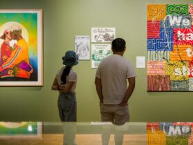 Two people stand in a green-walled gallery space with paintings on the walls.