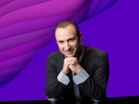 Simon Trpčeski (piano) is smiling at the camera with his hands clasped together under his chin
