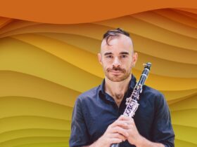 Ashley Smith is smiling directly at the camera holding his clarinet against his shoulder