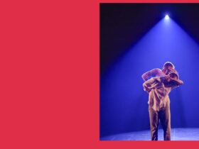 Two people dancing. One is standing behind the other. They are wearing beige linen clothes.