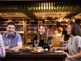 Three people sitting around a table with wine.