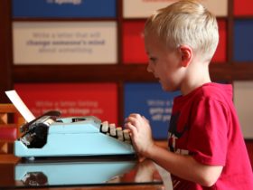 Young boy in red shirt typing at light blue typewriter in MoAD’s Yours Faithfully exhibition space